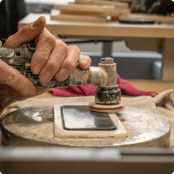 Das refurbished Smartphone liegt eingeklemmt in einer weissen Vorrichtung. Zwei Hände polieren das iPhone mit einer speziellen Bürste.